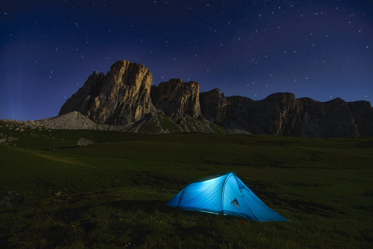 Camping under the starlit sky in the Dolomites, with a view of rugged cliffs in Italy.