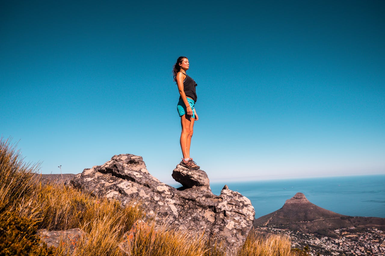 An adventurous woman stands confidently on a rock, overlooking the scenic landscape of Cape Town.